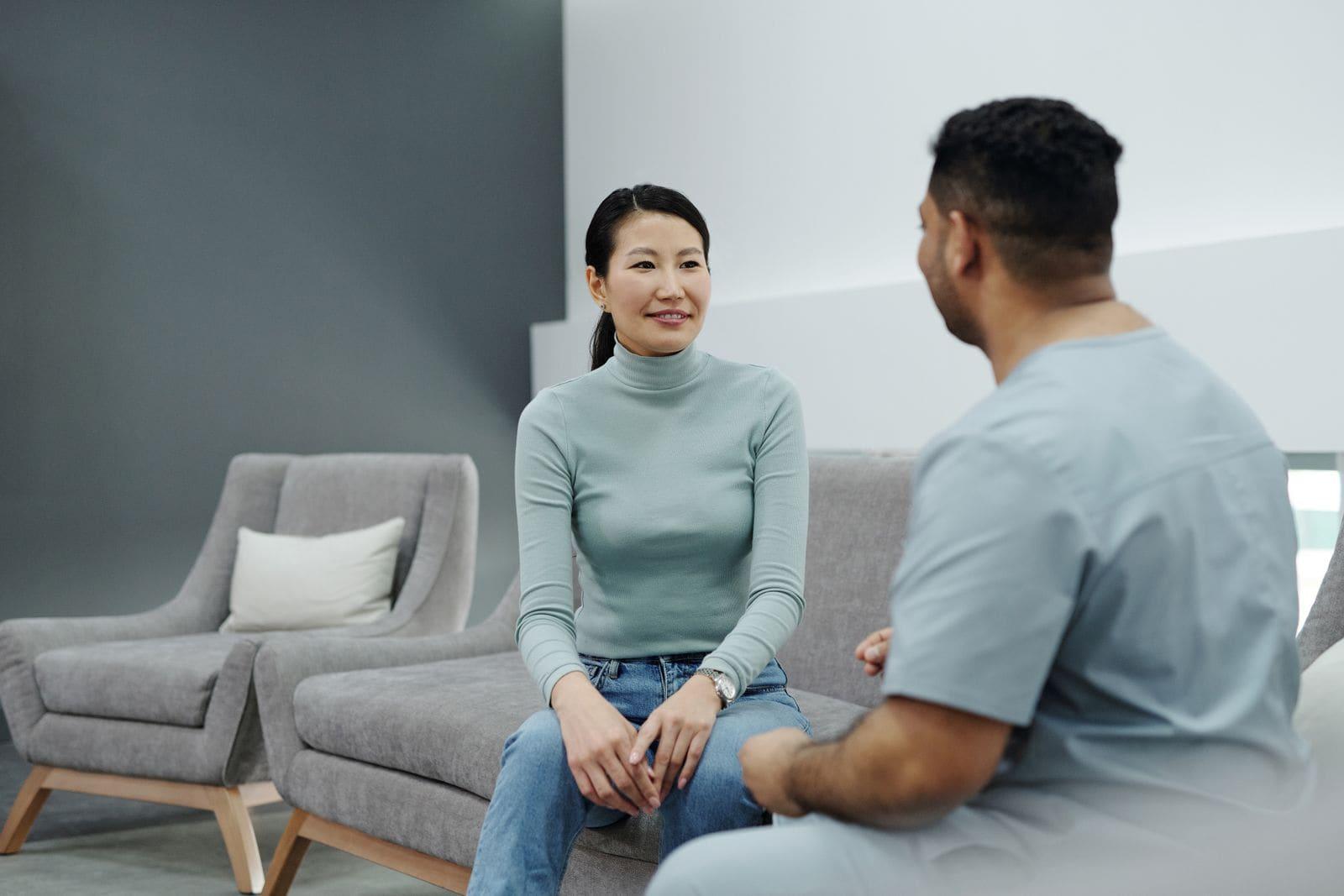 A patient and a clinician in scrubs talking side by side in a bright consulting room
