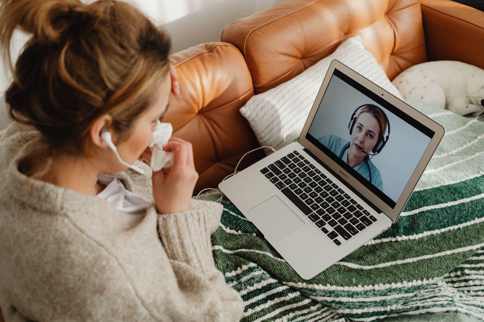 A woman at home on a video consultation, a clinician visible on her laptop screen