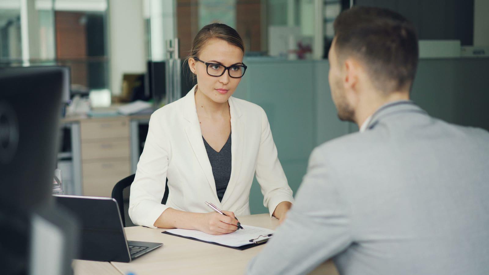 An adviser taking notes while a client talks, across a desk in a bright office