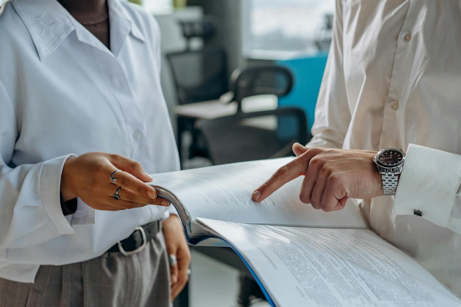 Two people going through a bound document together, one pointing at a clause