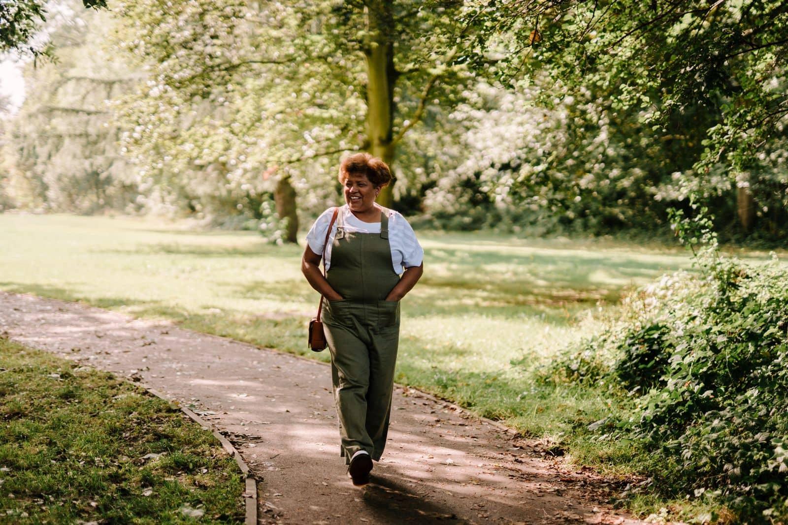 A woman walking a sunlit path through a park