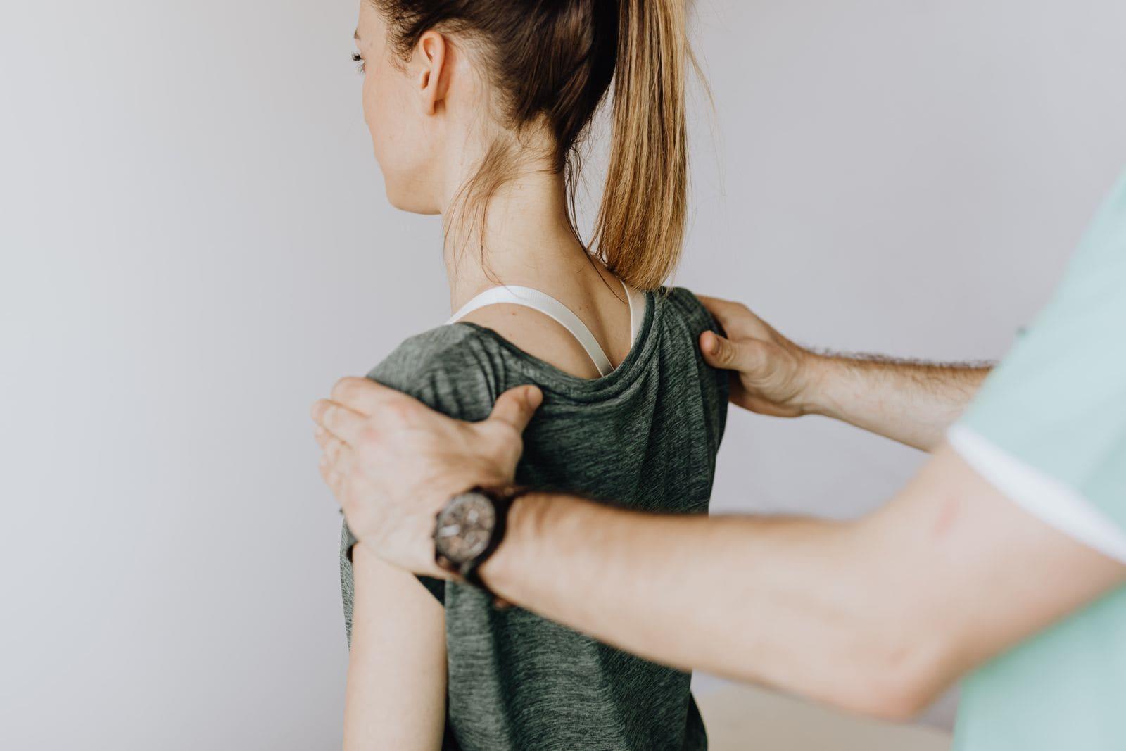 A physiotherapist's hands checking a patient's shoulder and upper-back posture