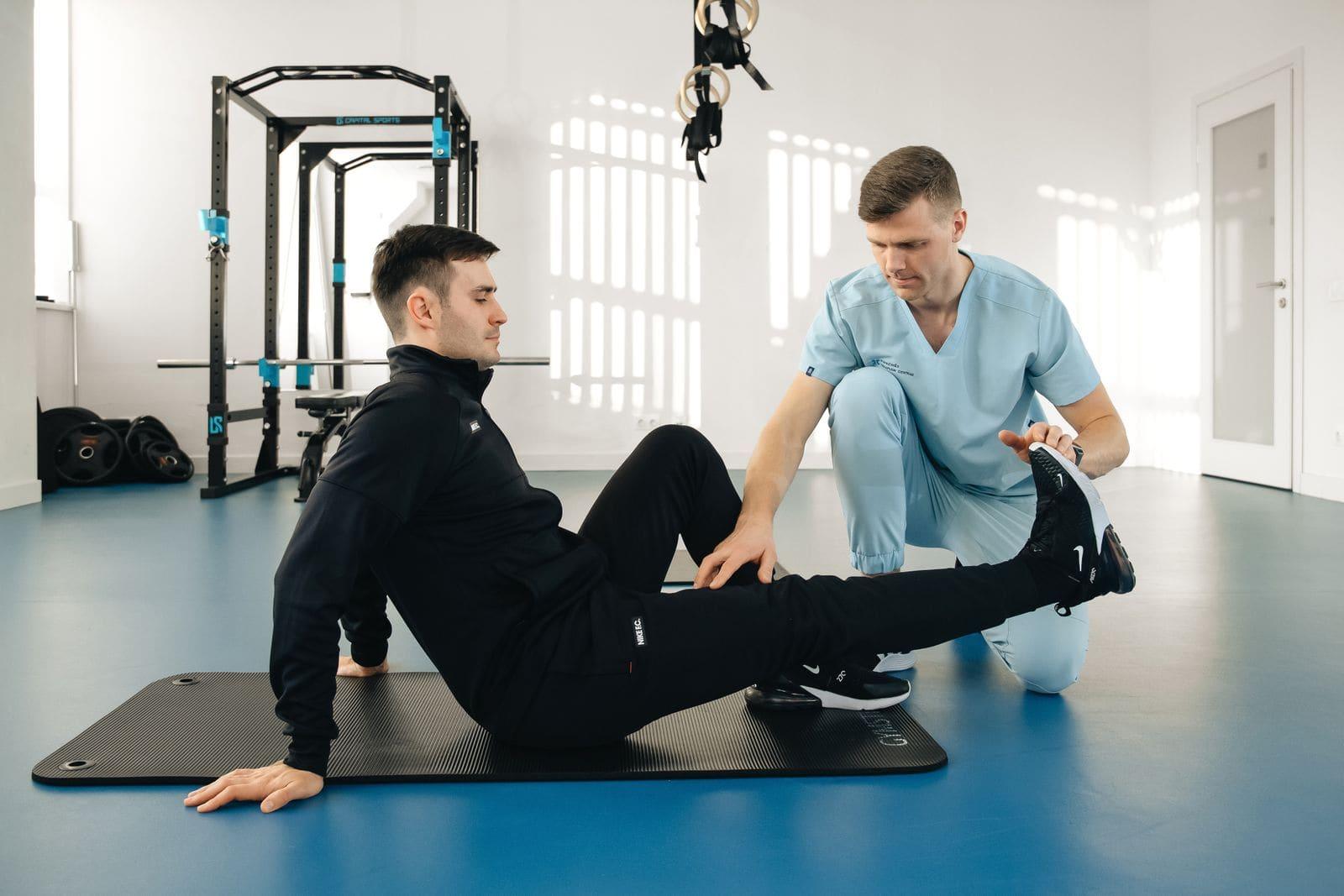 A clinician guiding a patient through a supervised stretch on an exercise mat in a rehab gym