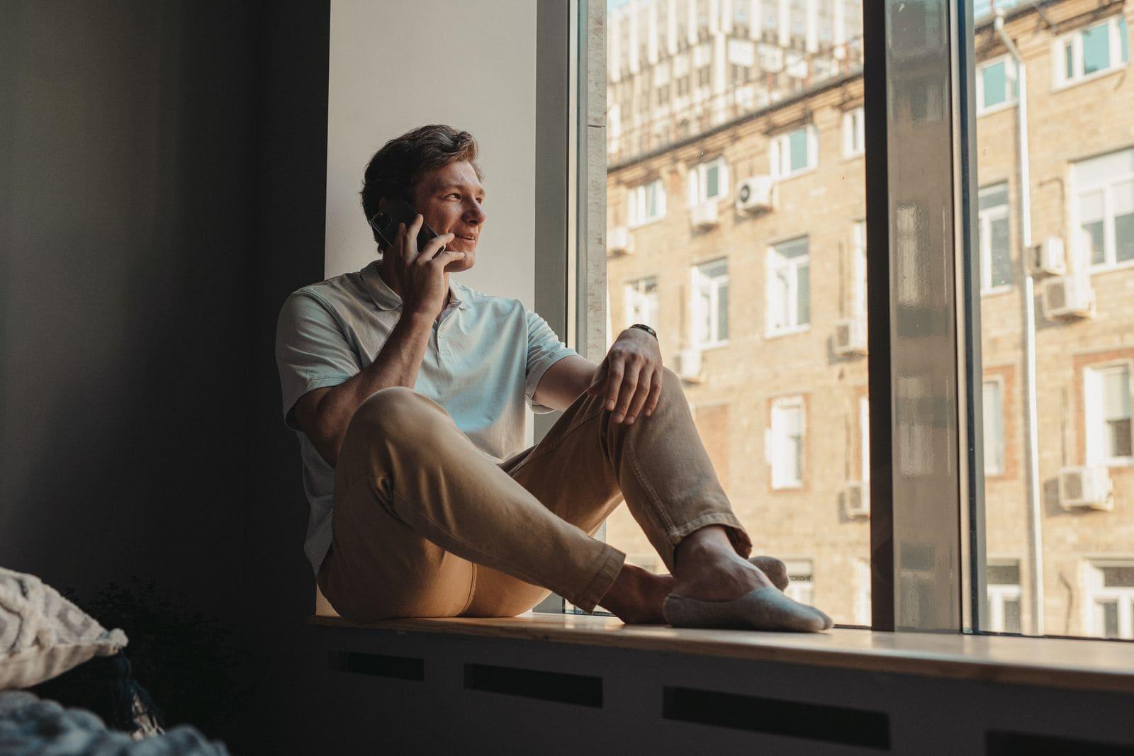 A man taking a phone consultation at home, sitting by a sunlit window