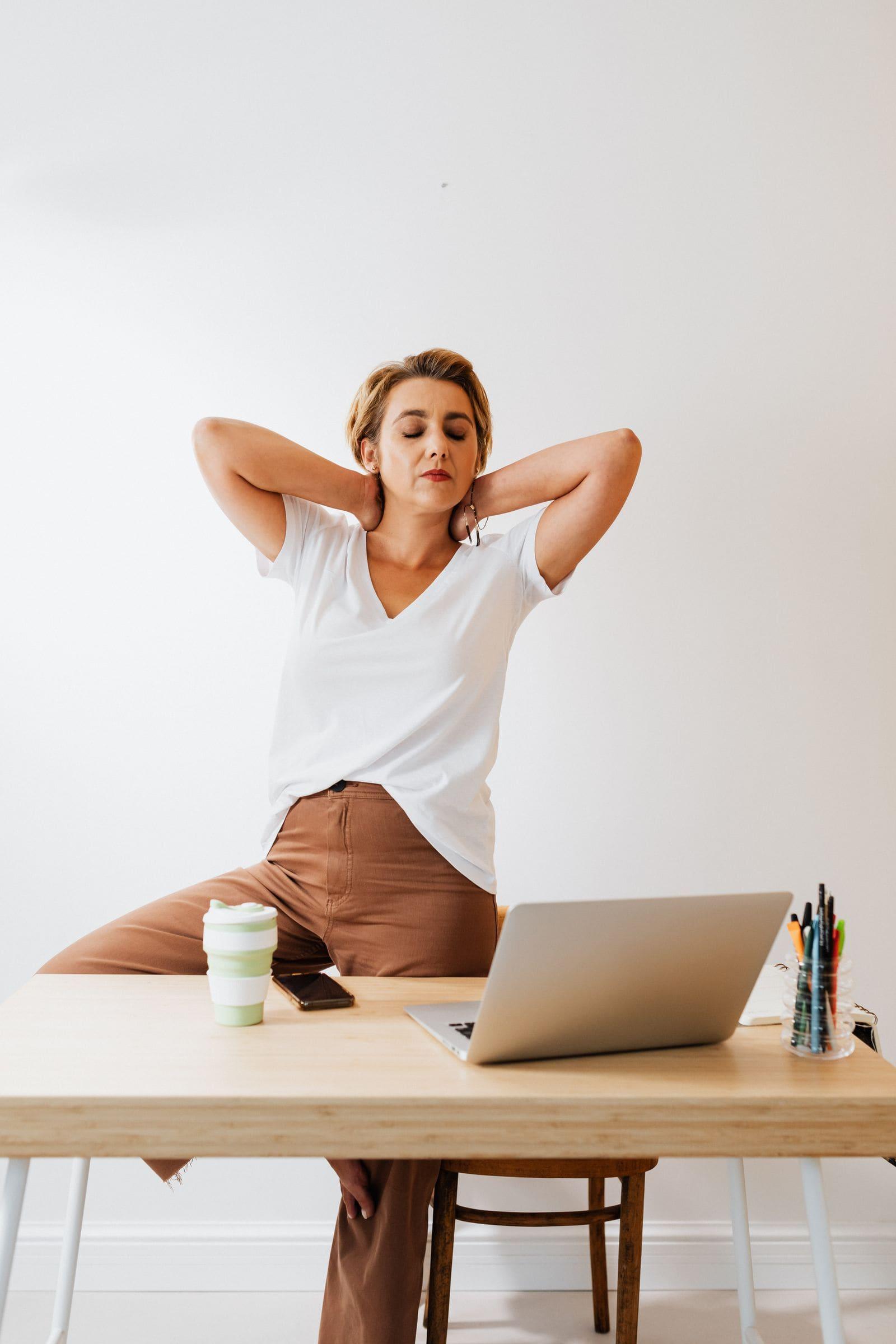 An office worker pausing at her desk, hands on the back of her neck